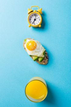 Flat lay with healthy sandwich with fresh avocado and fried quail egg on blue background. Breakfast or lunch food concept with copy space. Top view.