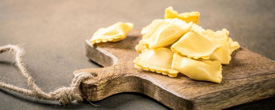 Fresh homemade italian stuffed square pasta ravioli on wooden cutting board. Healthy food concept, gluten free. Copy space.