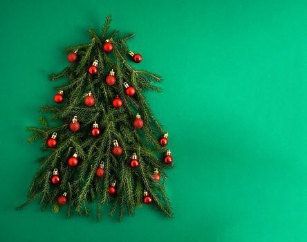 Christmas tree made of green coniferous branches on a green background. Christmas background with place for text. Christmas holiday concept. Ball toys. Red balls