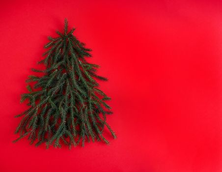 Christmas tree made of green coniferous branches on a red background. Christmas background with place for text. Christmas holiday concept. Card for new year. December mood