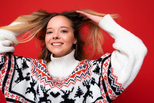 Young beautiful woman. Trendy woman in casual winter sweater. Positive female shows facial emotions. Funny model isolated on red background.