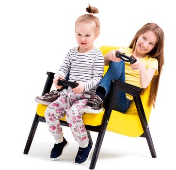 Siblings sitting in yellow leather chair playing battles with joystick, having fun