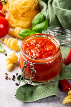 Glass jar with homemade classic spicy tomato pasta or pizza sauce with pine nuts and basil. Italian healthy food background.