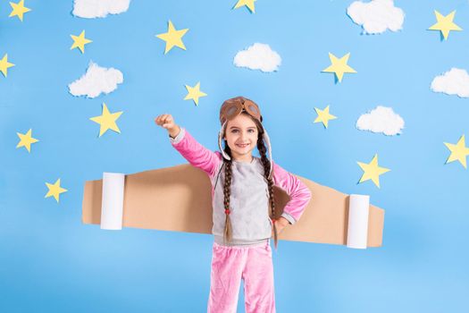 Little child girl in an astronaut costume is playing and dreaming of becoming a spaceman. Portrait of funny kid on a background of bright blue wall with yellow stars.