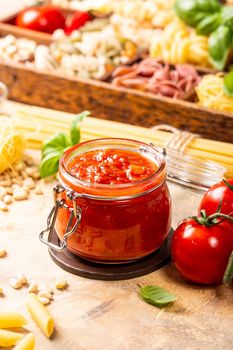 Glass jar with homemade classic spicy tomato pasta or pizza sauce with pine nuts and basil. Italian healthy food background.