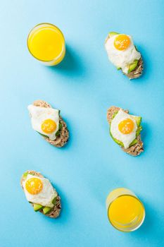 Flat lay with healthy sandwich with fresh avocado and fried quail egg on blue background. Breakfast or lunch food concept with copy space. Top view.