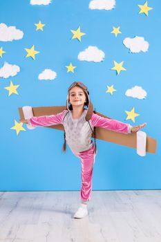 Girl pilot playing with toy jet pack at home. Success and leader concept. Kid on the background of bright blue wall with white clouds and yellow stars.