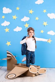 Little dreamer girl playing with a cardboard airplane at the studio with blue sky and white clouds background. Childhood. Fantasy, imagination.