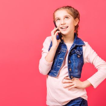Young little girl speaking on the mobile phone while standing in front of pink background
