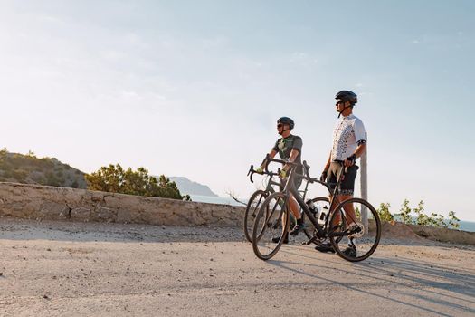 Two male cyclists stand on the coastal road and have a rest