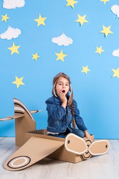 Little child girl in a pilot's costume is playing and dreaming of flying over the clouds. Portrait of funny kid on a background of bright blue wall with yellow stars and white clouds