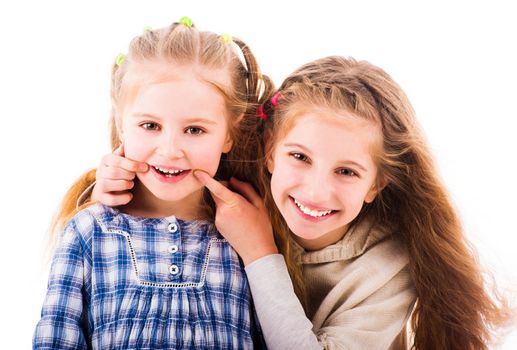 Girl put her fingers to the corners of the mouth to make her little sister smile. Two sisters having relaxing time together isolated on white background