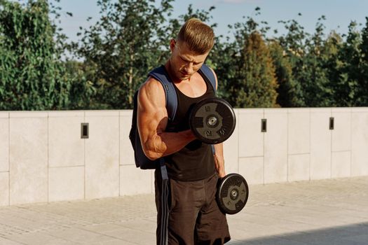 athletic man in black t-shirt with dumbbells in the park training. High quality photo