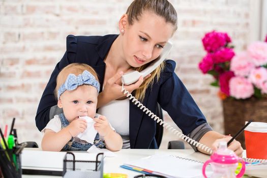 Family Business - telecommute Businesswoman and mother with kid is making a phone call. At the workplace, together with a small child