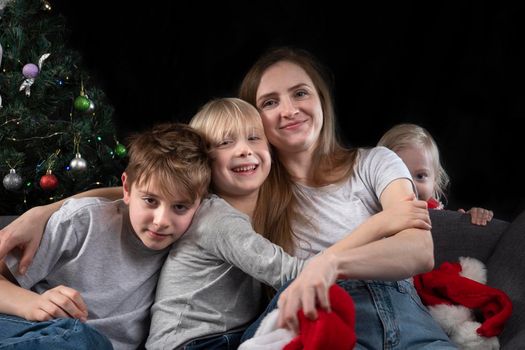 Portrait of young mother and three children at home on Christmas tree background