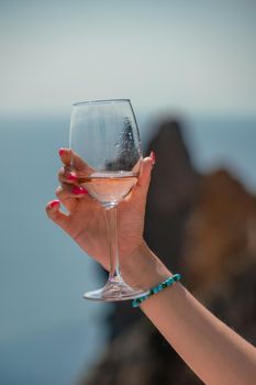 A female hand holds a glass of wine against the background of the sea and mountains