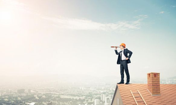 Young businessman in suit and helmet on roof edge. Mixed media