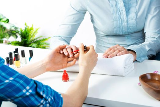 Manicurist working with client's nails at table. Closeup of beautiful female hands applying red nail polish in beauty salon. Professional nail care and beautician procedure in beauty center.