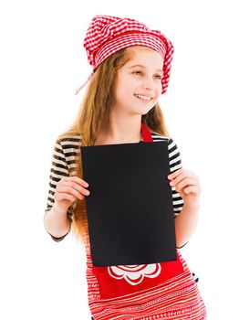Young little girl in red chef uniform holds vertical blank black sheet of paper and smiles isolated on white background. Copyspace, space for your text, recipe, advertising, menu