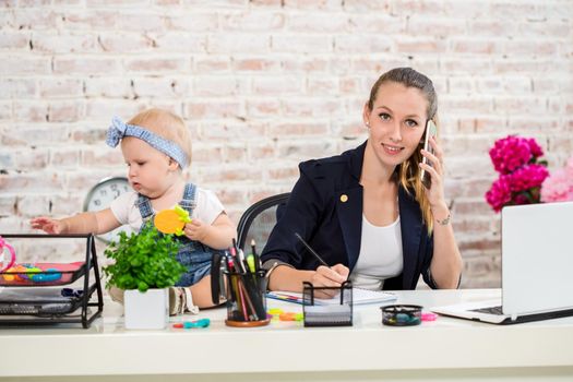 Family Business - telecommute Businesswoman and mother with kid is making a phone call. At the workplace, together with a small child