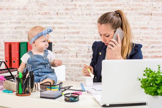 Family Business - telecommute Businesswoman and mother with kid is making a phone call. At the workplace, together with a small child