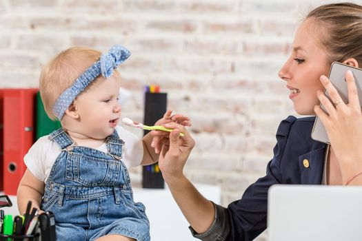 Family Business - telecommute Businesswoman and mother with kid is making a phone call. At the workplace, together with a small child