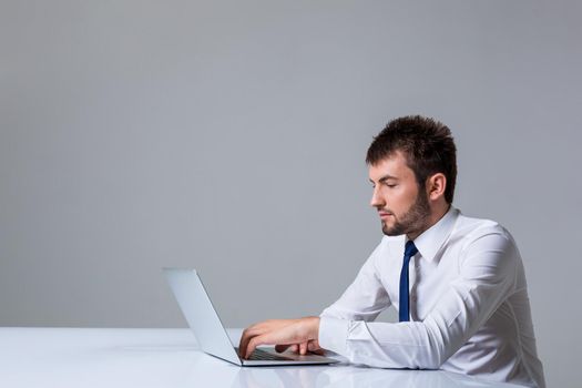 young man smiling at the camera uses a laptop computer while sitting at a table. Office clothing. copyspace