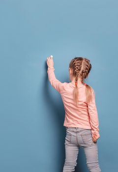 Little girl in casual clothes writes with chalk on blue background