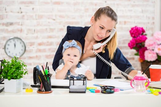 Family Business - telecommute Businesswoman and mother with kid is making a phone call. At the workplace, together with a small child