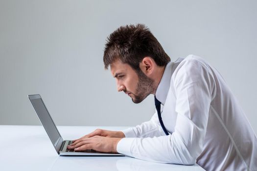 nerd young male typing on laptop. It uses a computer while sitting at a table. Office clothing