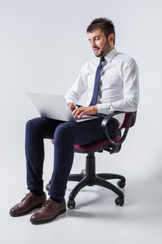 emotional young guy in office clothes working on a laptop computer and sitting on a chair