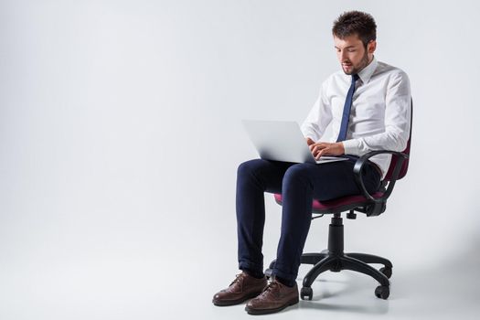 emotional young guy in office clothes working on a laptop computer and sitting on a chair