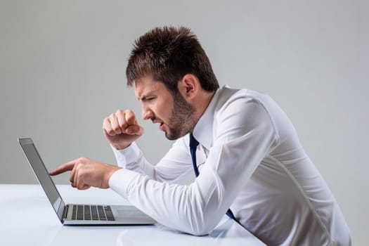 the young man is nervous and poke a finger. It uses a computer while sitting at a table. Office clothing