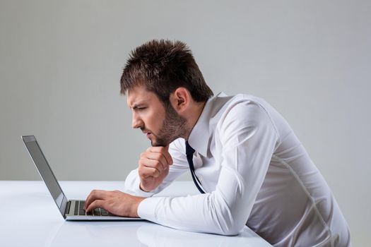 the young man stares at a laptop. It uses a computer while sitting at a table. Office clothing