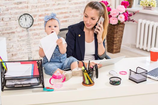 Family Business - telecommute Businesswoman and mother with kid is making a phone call. At the workplace, together with a small child