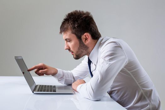young man presses the laptop. It uses a computer while sitting at a table. Office clothing