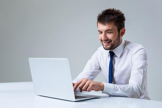 young man smiling and typing using laptop computer sitting at the table. Office clothing