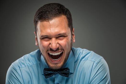 Portrait of happy smiling young man in blue shirt and butterfly tie isolated over gray studio background. Closeup