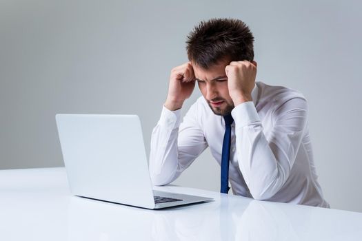 young man frustrated using laptop computer sitting at the table. Office clothing