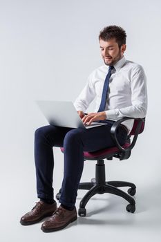 emotional young guy in office clothes working on a laptop computer and sitting on a chair