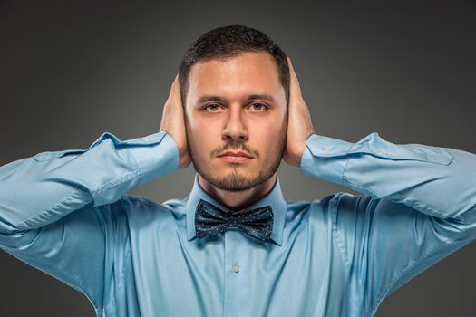 Portrait young man in blue shirt and butterfly tie looking at the camera, hands raised, isolated on gray studio background. Human emotion, facial expression. Closeup