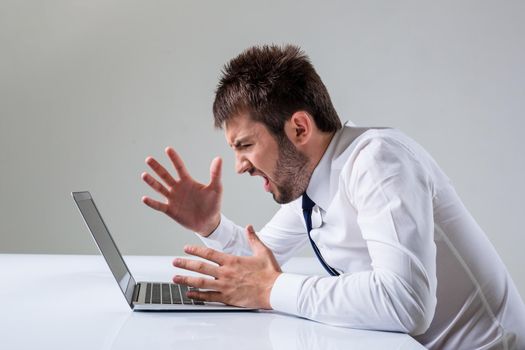 the young man is nervous. It uses a computer while sitting at a table. Office clothing