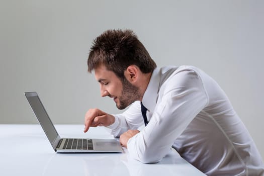 young man presses the keyboard on a laptop bully. It uses a computer while sitting at a table. Office clothing