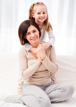 Portrait of happy mother and daughter hugging and smiling at camera in the living room