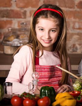 Beautiful little girl in red apron cooking vegetable salad at home
