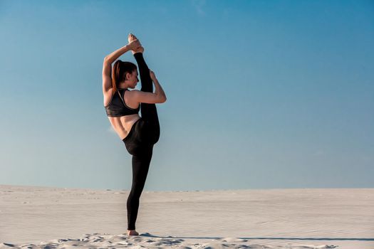 Young slim woman do gymnastic exercise at white sand beach under blue sky. Young gymnast on seashore