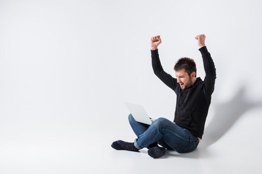 a young man in casual clothes working on a laptop. glad hands up