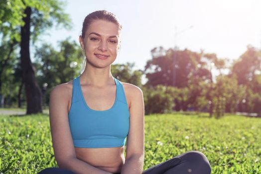 Girl meditates in lotus pose on green grass. Practicing of yoga at summer park. Portrait of young peaceful woman. Training and meditation outdoor at summer day. Healthy lifestyle and relaxation.