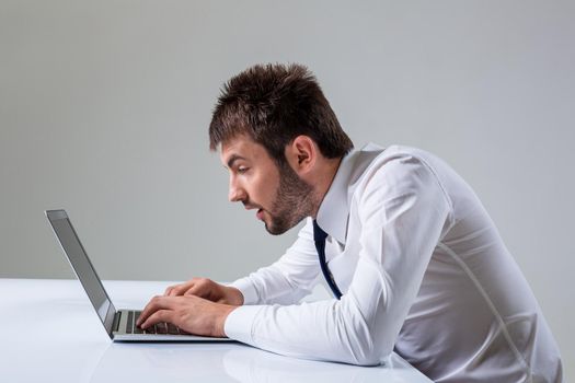 nerd young male surprise and typing on laptop. It uses a computer while sitting at a table. Office clothing