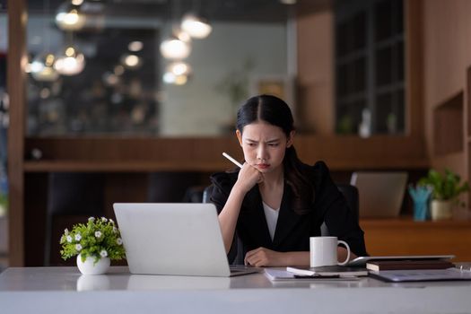 asian business woman thinking solving problem at work, worried serious young asian woman concerned make difficult decision lost in thought reflecting sit with laptop